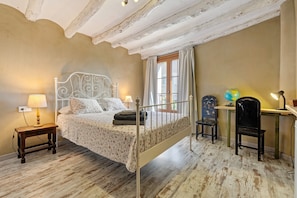 Un dormitorio con cama, mesita de noche, lámpara, silla, escritorio, globo terráqueo y ventana.