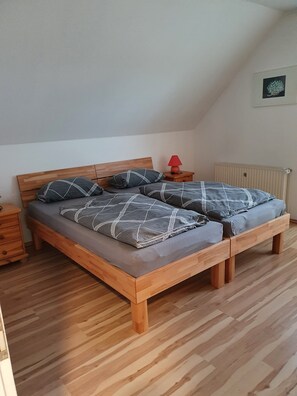 En træseng med grå madras og mønstrede puder, en rød lampe på et natbord, og en radiator på væggen.