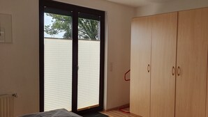 Quarto com porta de vidro deslizante, guarda-roupa de madeira e radiador.