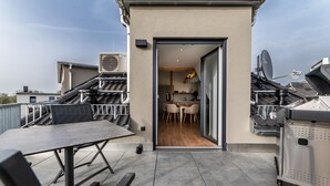 Une terrasse sur le toit, avec une table et des chaises, un barbecue et une antenne parabolique.
