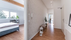 Une chambre moderne avec un lit, un plancher en bois, une grande fenêtre et un couloir menant à une autre pièce.