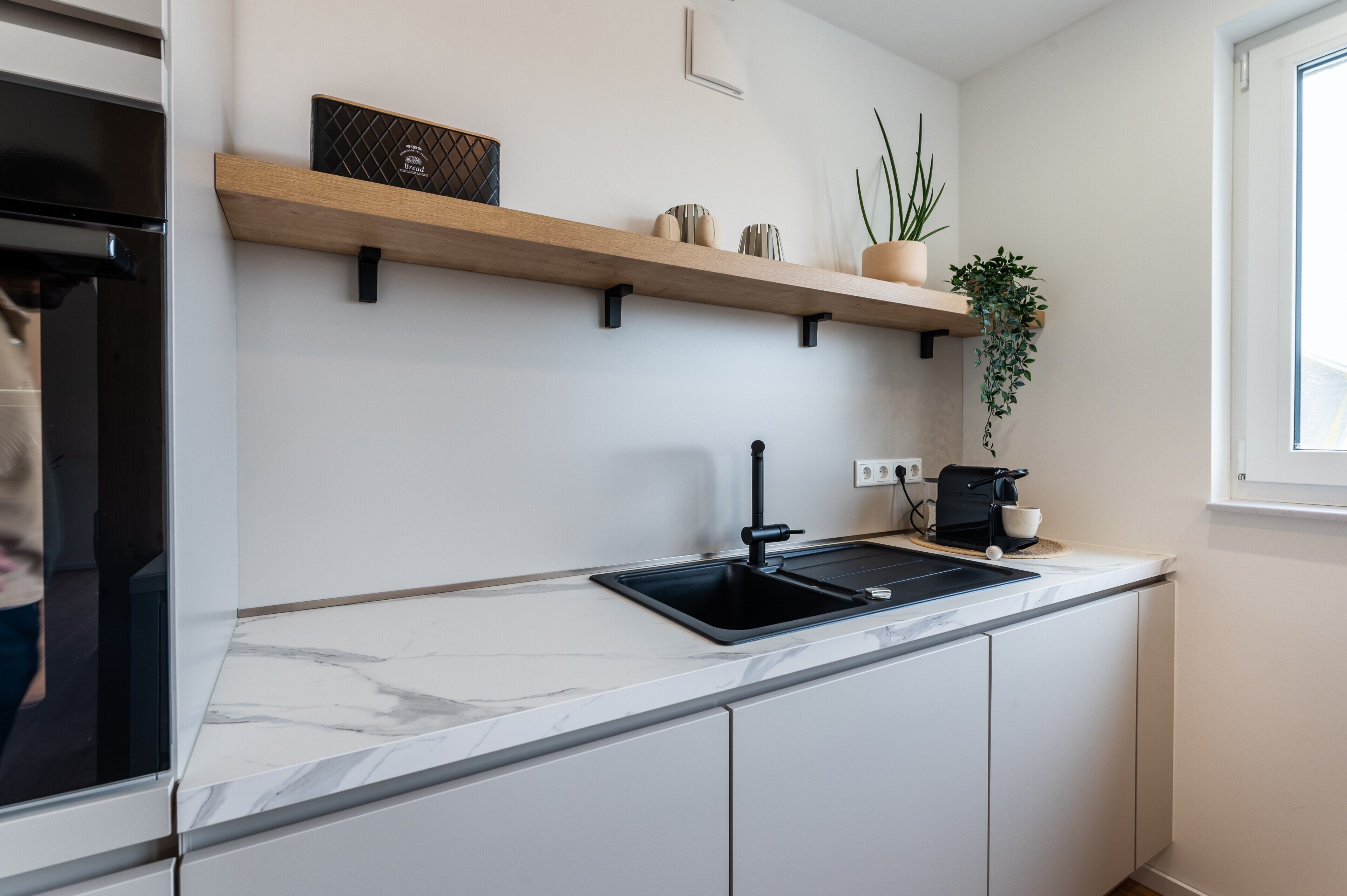 Una cucina moderna con un piano di lavoro in marmo, un lavello nero e una mensola in legno con oggetti decorativi.