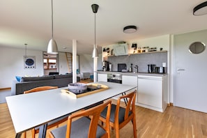 A modern kitchen with white cabinets, a dining table with chairs, and pendant lighting. - ‘ Stille des Nordens ’ is a spacious holiday flat approx. 68sqm 3 persons on the upper floor (Pellworm)