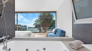 A modern bathroom with a large bathtub, a shower, and a view of the sea.