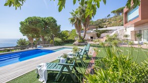 A pool area with a wooden deck, lounge chairs, and a view of the sea. - Holiday Home 'Yaiza' with Sea View, Wi-Fi and Air Conditioning (Lloret de Mar)