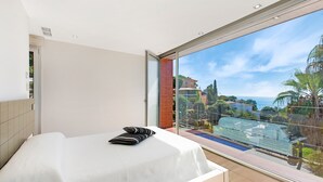 A hotel room with a large balcony, a bed, and a view of the sea and buildings.
