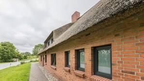 Un edificio de ladrillo con techo de paja, un sendero pavimentado y una zona ajardinada.
