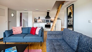 Una sala moderna con sofá y una mesa de centro, una cocina con electrodomésticos y una escalera.