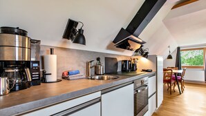 Una cocina moderna equipada con cafetera, hervidor y tostadora. Incluye un lavamanos, escurreplatos y una zona de comedor con mesa y sillas.