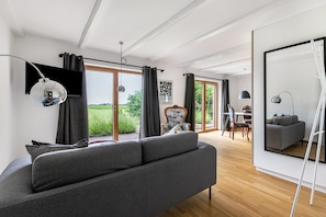 Un salon moderne avec un canapé, un coin repas comprenant une table et des chaises, et une grande fenêtre avec des rideaux.