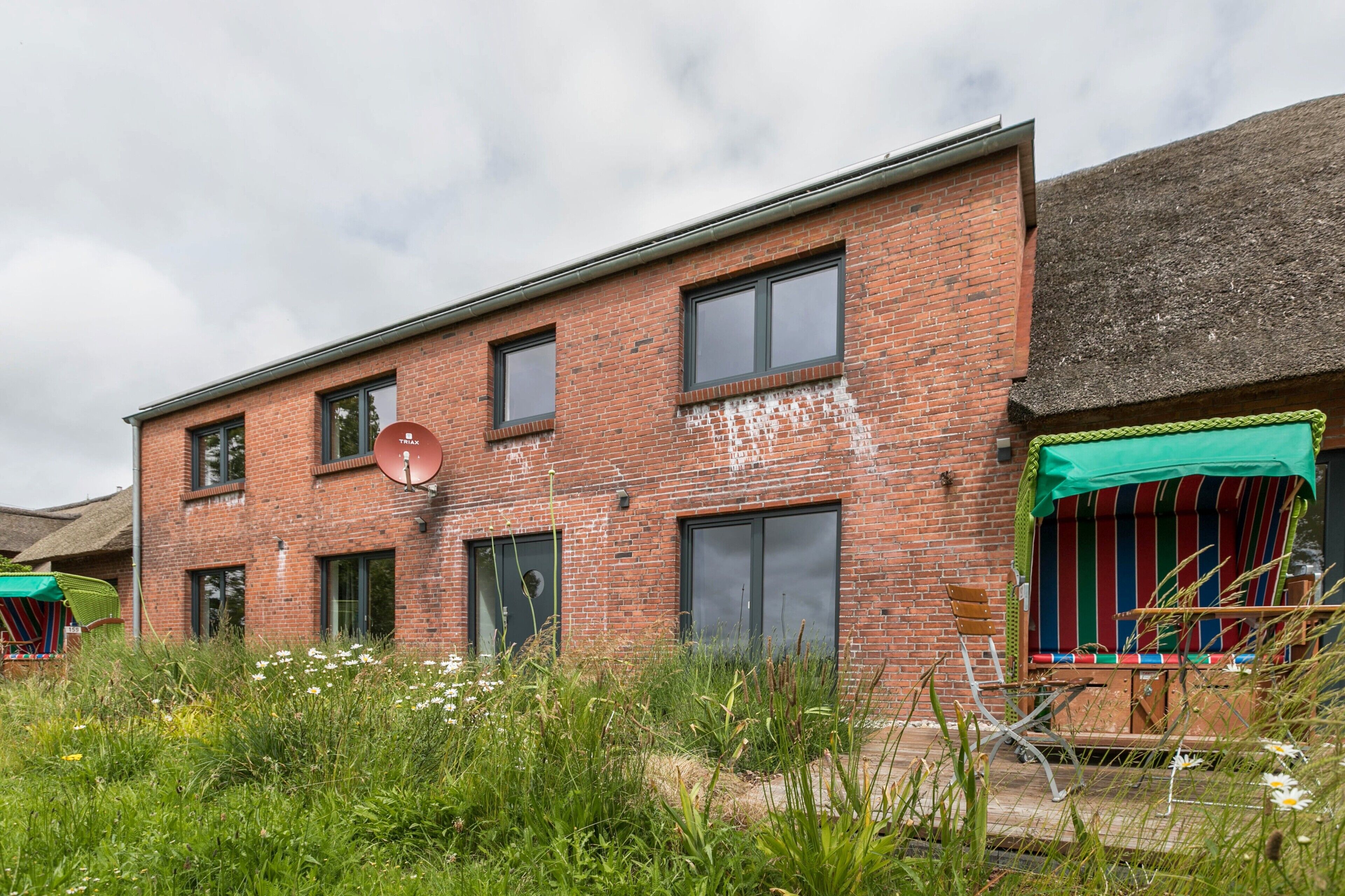 Een gebouw van rode bakstenen met meerdere ramen, een schotelantenne en een groene luifel boven een zitgedeelte.