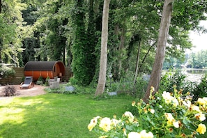 A wooden cabin with a sloped roof, surrounded by a lush garden and a lake view. - Apartment 'Ferienwohnung Bestensee' with Lake View, Private Terrace and Wi-Fi (Bestensee)