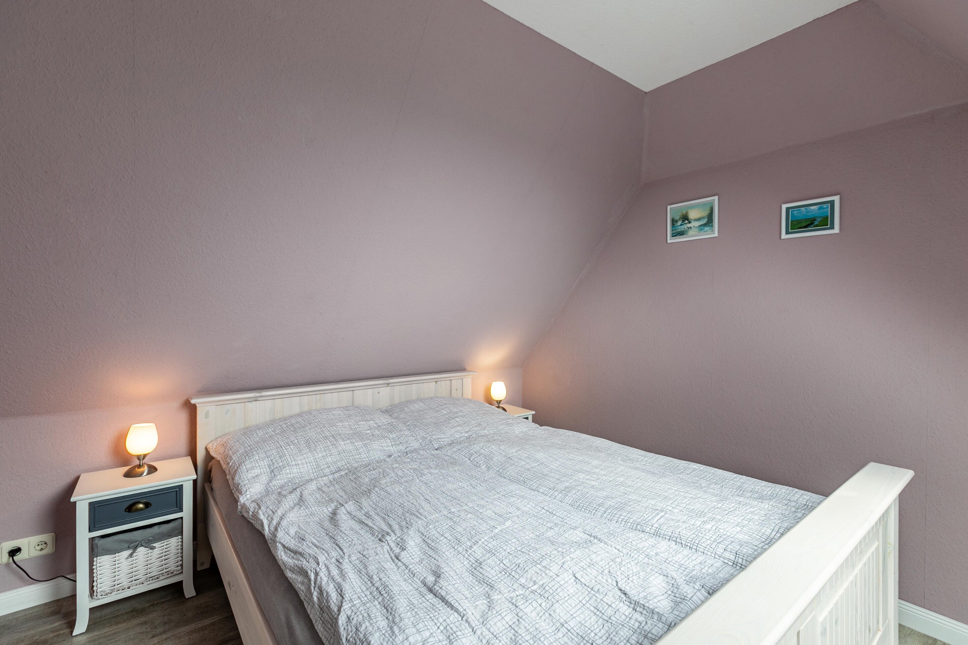 Une chambre à coucher avec un lit simple, des tables de chevet, une lampe et deux tableaux encadrés au mur.