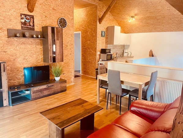 A cozy living room with a TV, wooden furniture, a red sofa, and a kitchen area with a dining table and chairs. - Holiday Home 'Alter Stall' with Private Terrace, Private Garden and Wi-Fi (Oberuckersee)