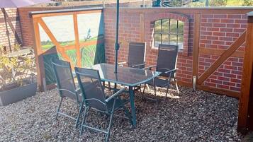 A patio with a table and chairs, a blue umbrella, and a brick wall.