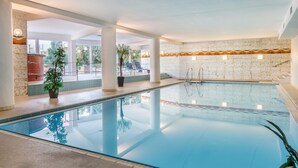 Une piscine intérieure à l’eau claire, entourée de colonnes et de plantes en pot.