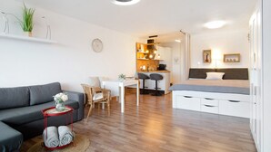 Un salon moderne avec un canapé gris, une table à manger et un coin cuisine à l’arrière-plan.