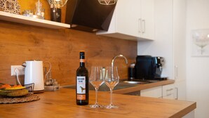 Un comptoir de cuisine avec une bouteille de vin, deux verres et un panier de fruits.