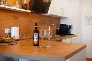 Un comptoir de cuisine avec une bouteille de vin, deux verres et un panier de fruits.