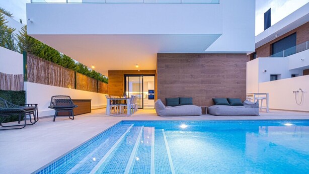 Un espace piscine extérieur moderne, doté d’un coin salon intégré, d’un mur en bois et d’une porte vitrée donnant accès à un espace intérieur.