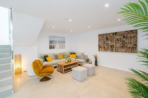 A modern living room with a sofa, ottomans, a coffee table, and a bookshelf.