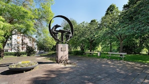 Un parc comprenant une sculpture circulaire, une allée pavée et un banc.