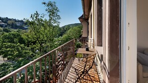 Un balcon donnant sur un paysage verdoyant, une table en bois et une chaise.