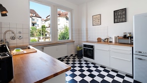 Une cuisine avec un carrelage à motifs, des placards blancs, une fenêtre et une vue sur les bâtiments environnants.