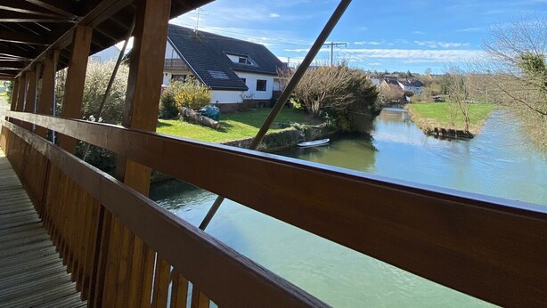 Een houten brug met uitzicht op een rivier en huizen op de achtergrond.