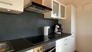 Een moderne keuken met een zwart aanrecht, roestvrijstalen apparatuur, witte kasten en een houten plafond.