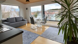 Een modern interieur met een houten plafond, een grijze bank, een eettafel met stoelen en een groot raam.