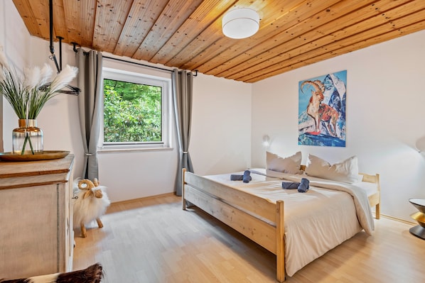 A bedroom with a wooden bed, a window with curtains, a painting on the wall, and a small cabinet. - Holiday Home 'Ferienhaus Sonnenplatz Am See' with Private Terrace (Roding)