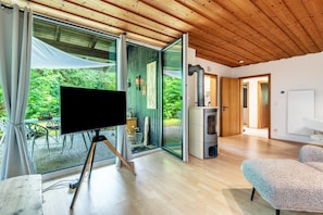 A modern interior with a TV on a tripod, a fireplace, and a sliding glass door to a garden. - Holiday Home 'Ferienhaus Sonnenplatz Am See' with Private Terrace (Roding)