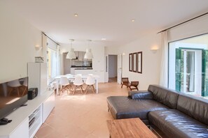 Een moderne woonkamer met een leren bank, een eethoek met witte stoelen en een keuken op de achtergrond.