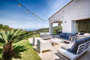 A modern outdoor patio with white furniture, a string of lights, and a view of the landscape.