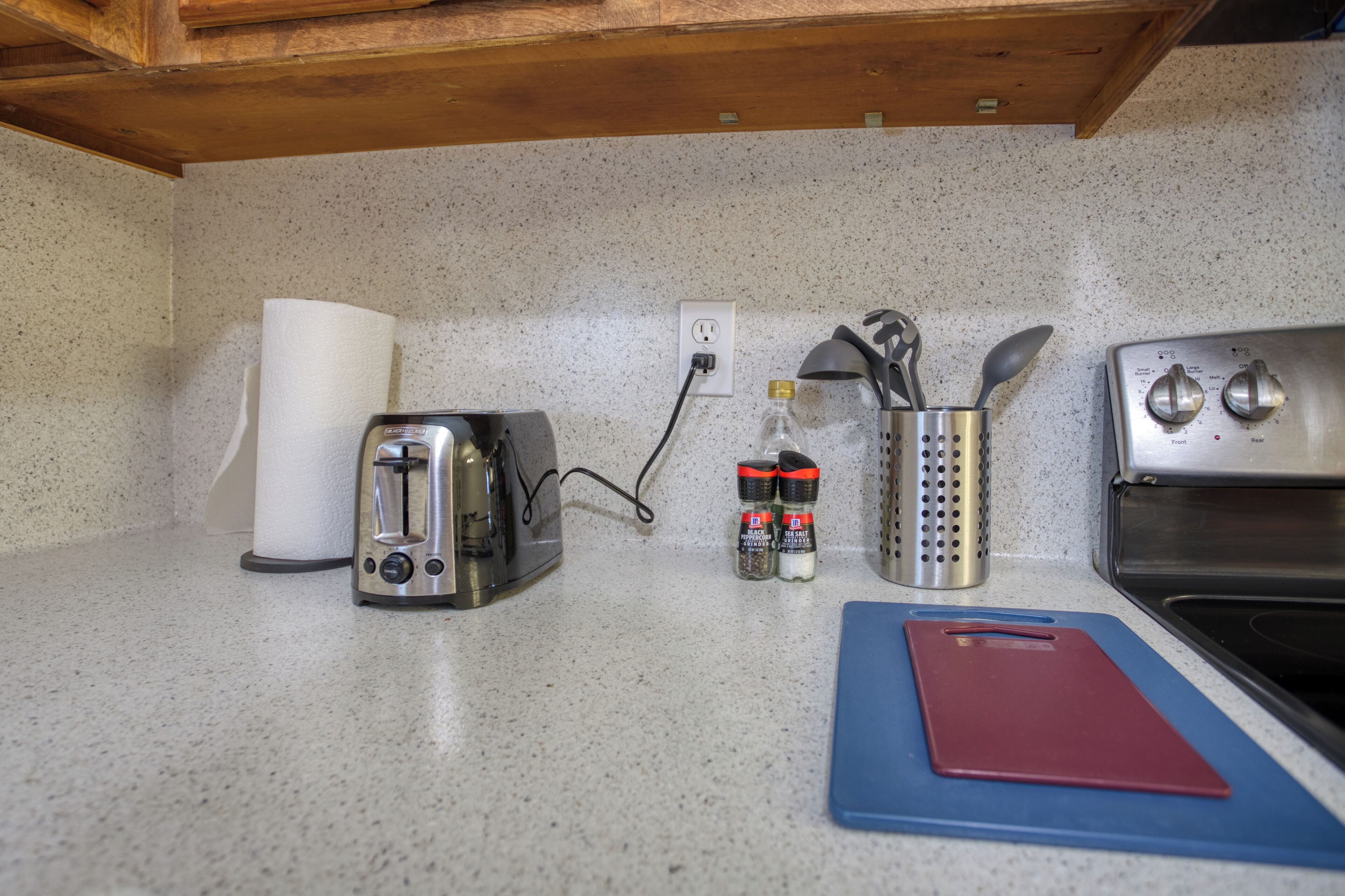 A kitchen counter with a toaster, paper towel holder, spice jars, a grater, and a cutting board.
