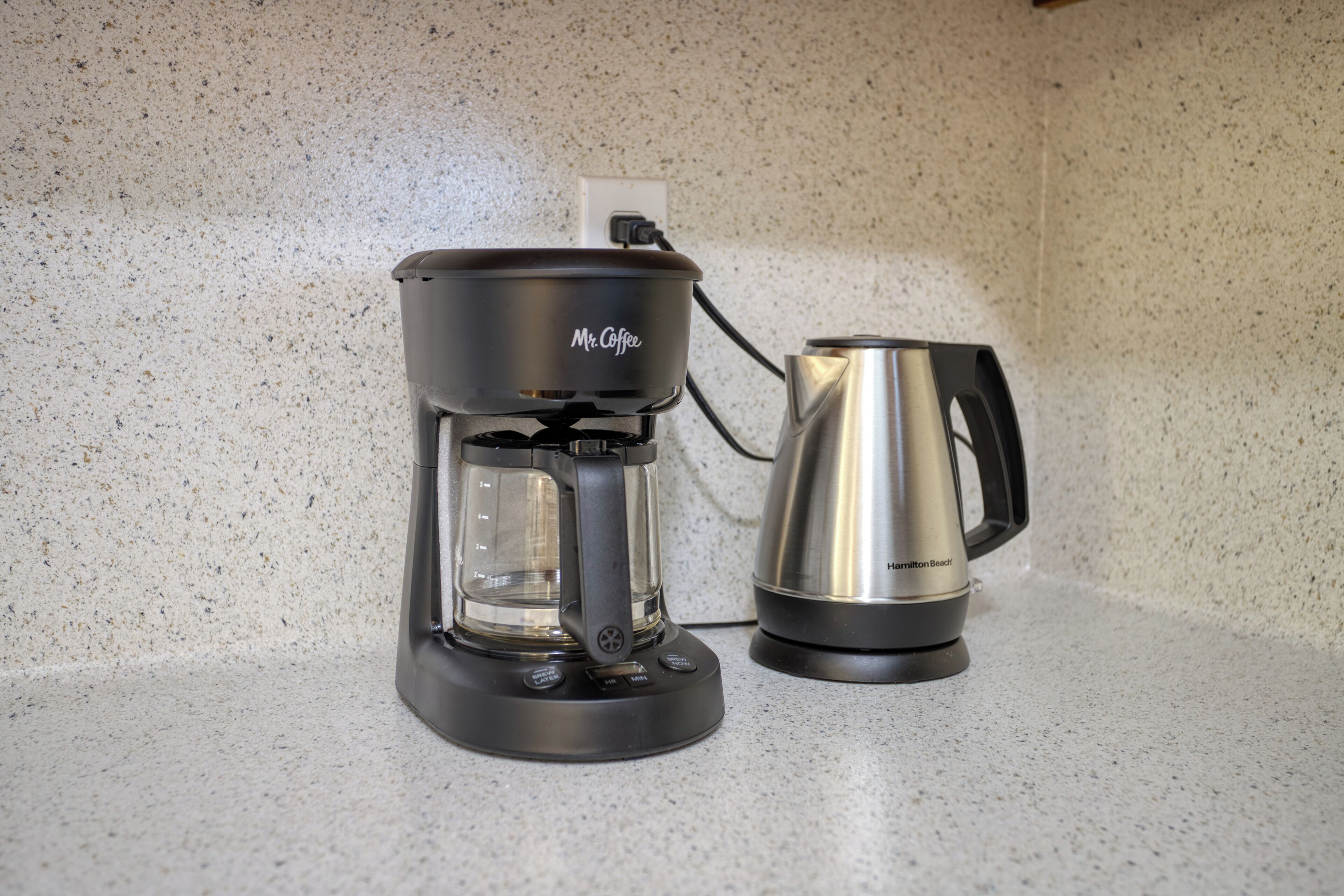Een Mr. Coffee koffiezetapparaat en een Hamilton Beach koffiekan op een gevlekt aanrecht.