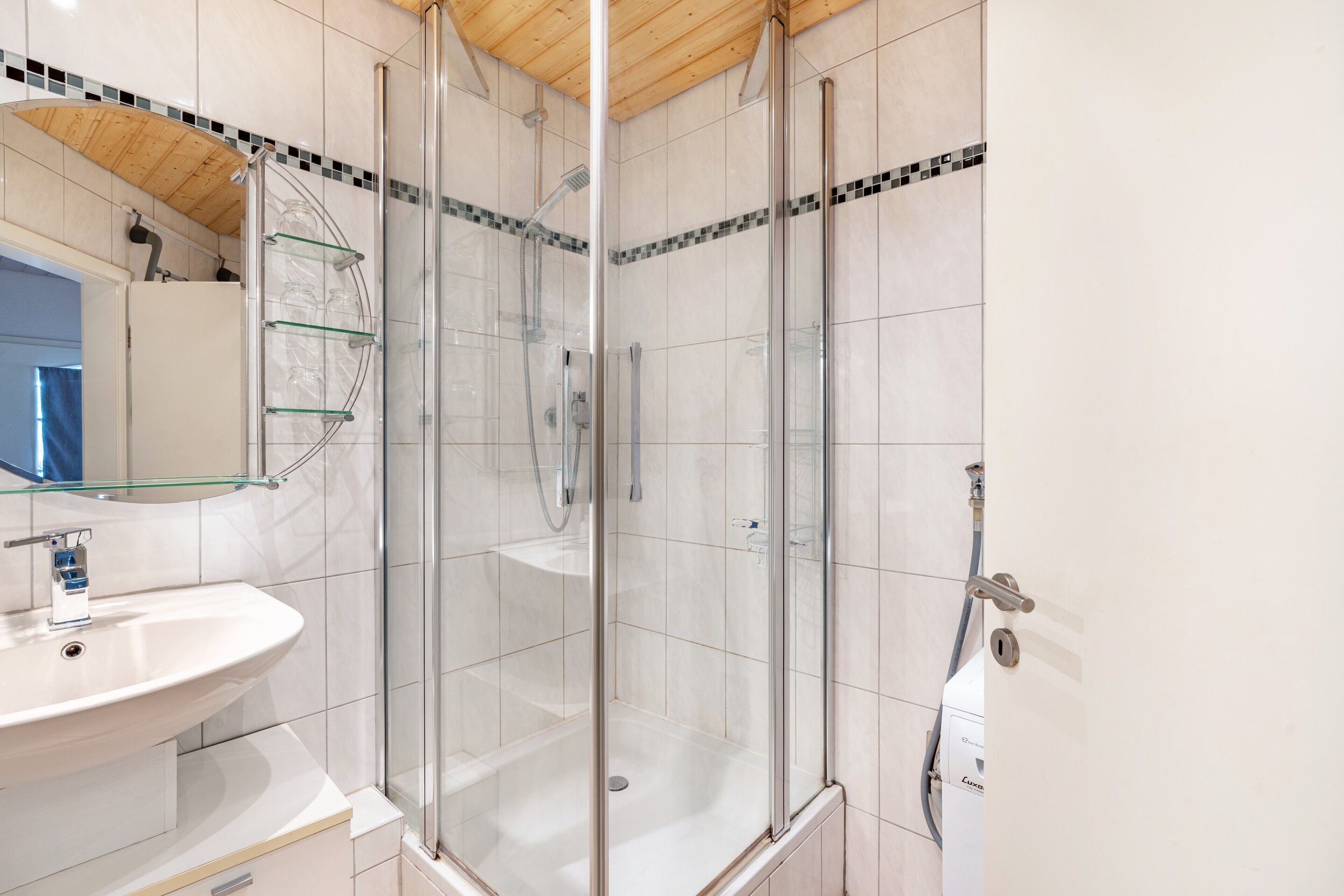 Ein modernes Badezimmer mit einer gläsernen Duschkabine, einem weißen Waschbecken und einem Spiegel.