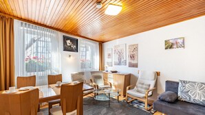 Ett modernt vardagsrum med ett träpanelat tak, ett soffbord i glas, en soffa och en matplats med stolar.
