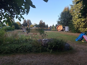 A garden with a wooden barrel structure, a playground slide, and a variety of plants.
