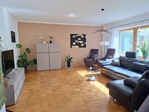 A modern living room with a sofa, chairs, a TV, and a refrigerator.