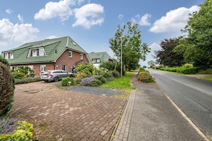 A residential street with houses, a paved driveway, and a parked car.