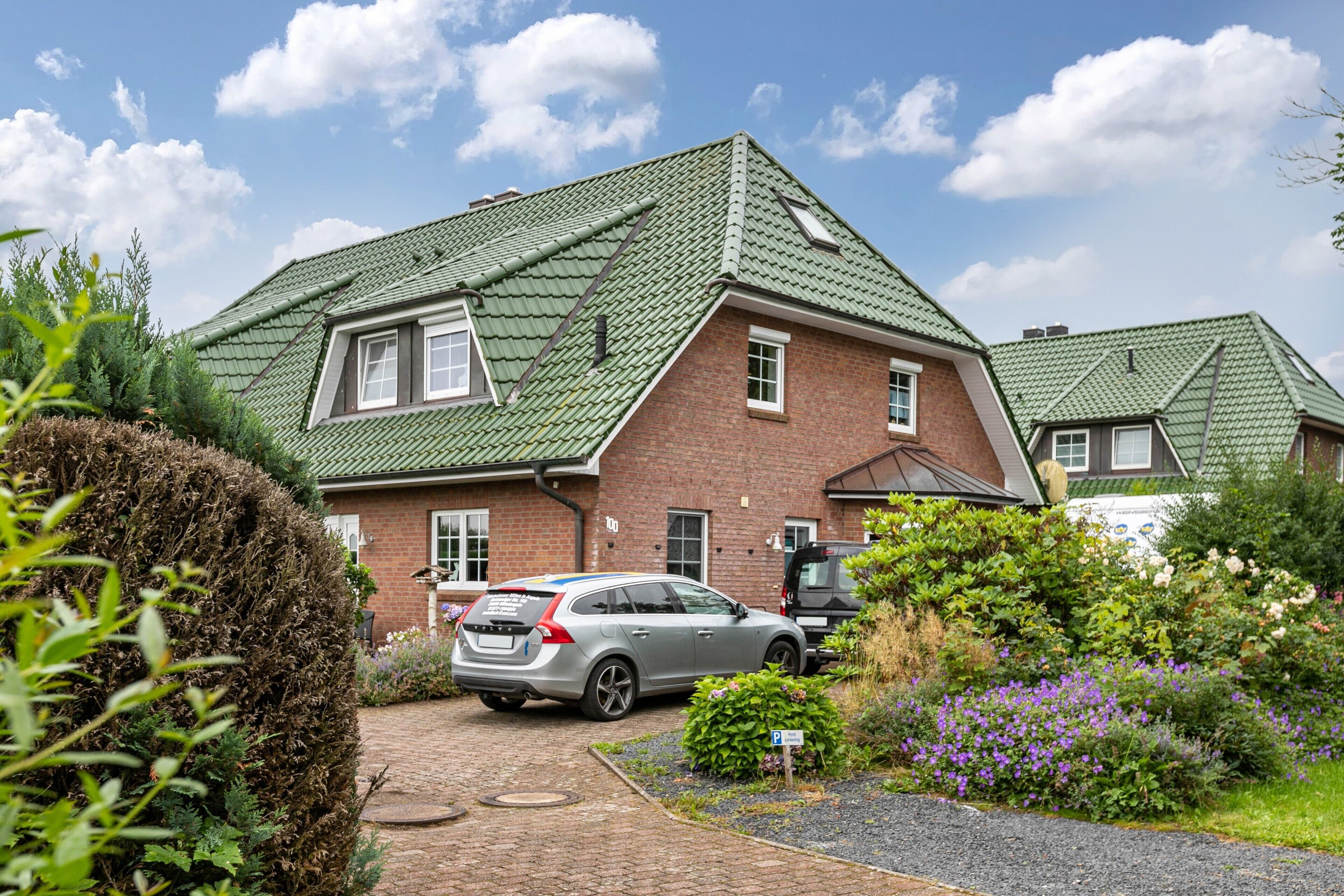Ein zweistöckiges Haus mit einem grünen Dach, einer gepflasterten Auffahrt und einem parkenden Auto.