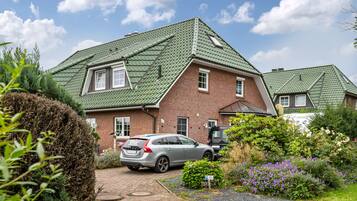 Ein zweistöckiges Haus mit einem grünen Dach, einer gepflasterten Auffahrt und einem parkenden Auto.