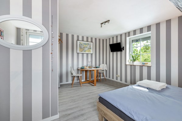 A bedroom with a bed, a desk, chairs, a TV, and a window.