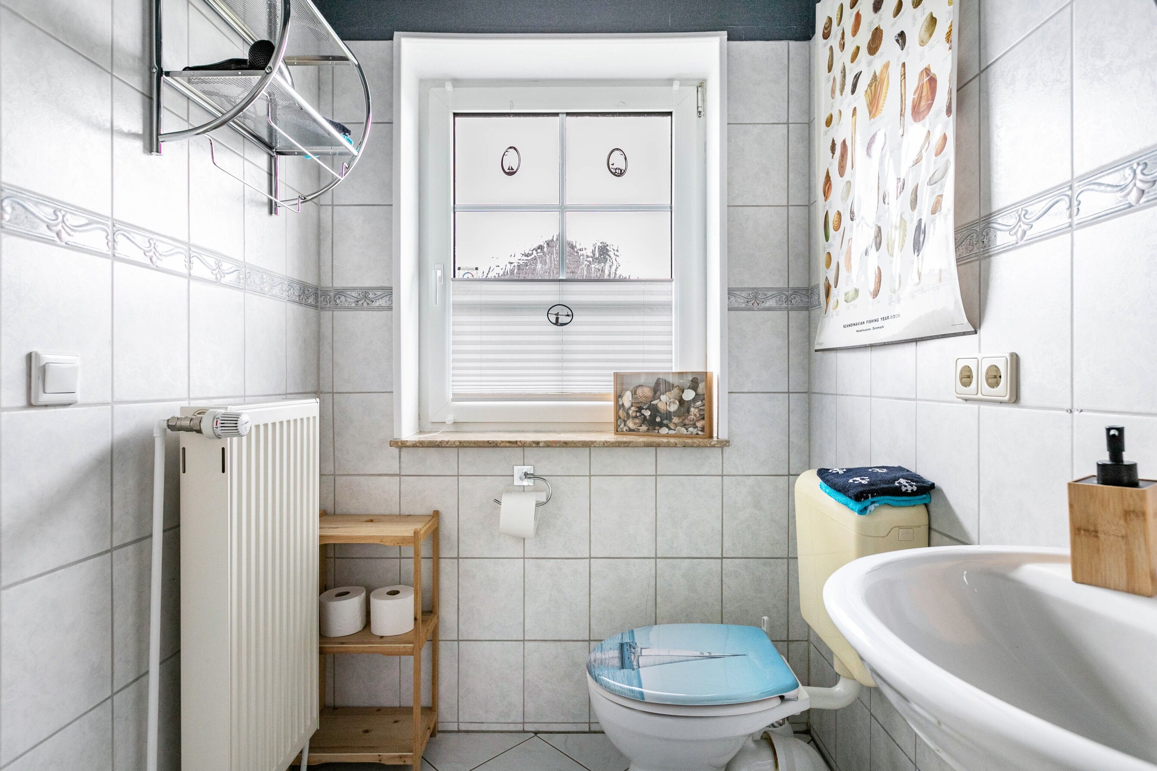 Ein Badezimmer mit Toilette, Heizkörper, Ablage für Toilettenartikel, Fenster mit Aussicht und Waschbecken.
