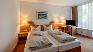 Une chambre d’hôtel avec deux lits, un bureau, une chaise, une télévision et un tableau au mur.