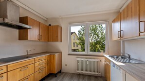 Une cuisine moderne avec des meubles en bois, une cuisinière encastrée, une fenêtre donnant sur une maison et un lave-vaisselle.