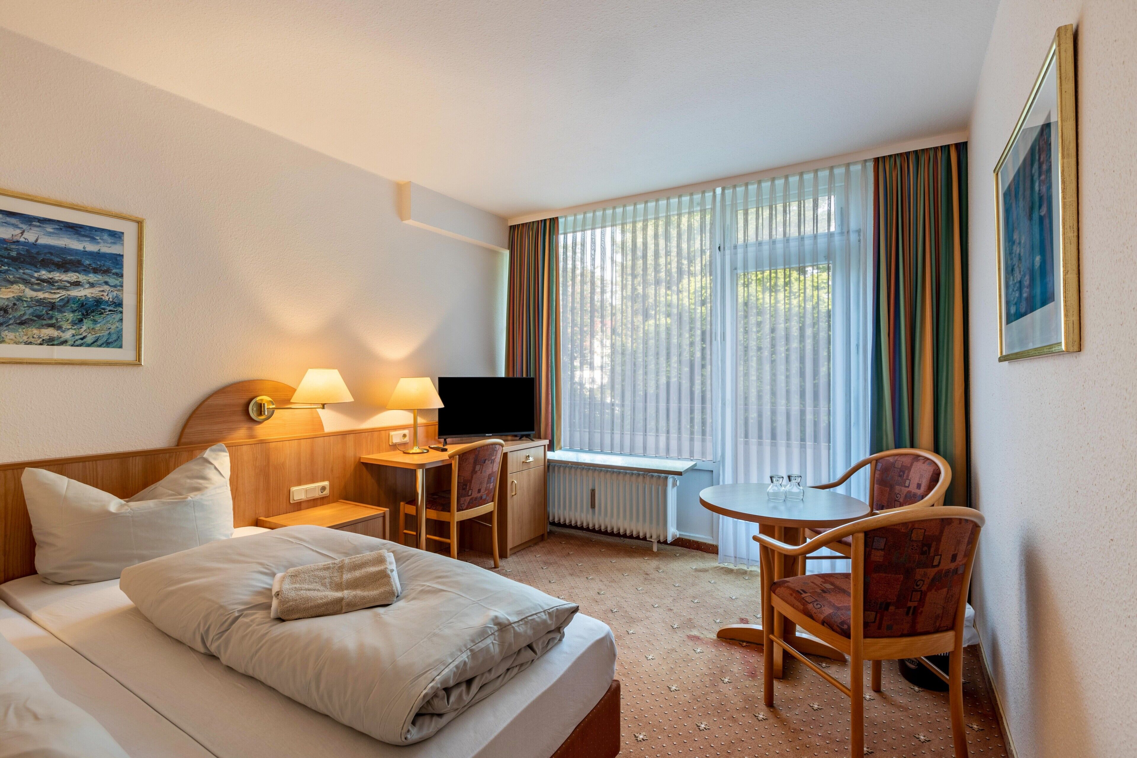 Ein Hotelzimmer mit Bett, Schreibtisch, Stuhl, Fernseher und einem Fenster mit Vorhängen.