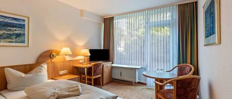 Ein Hotelzimmer mit Bett, Schreibtisch, Stuhl, Fernseher und einem Fenster mit Vorhängen.